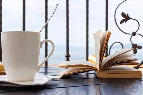 White coffee cup and open book on a balcony table overlooking the Adriatic .. Stock Photos