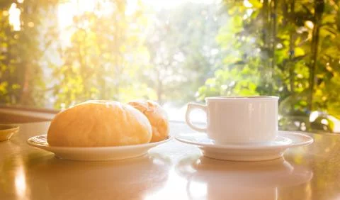 White coffee cup with bread on the table with sunlight in the background. 스톡 사진