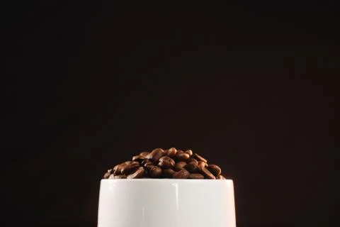 A white coffee cup filled with roasted dark coffee beans. Stock Photos
