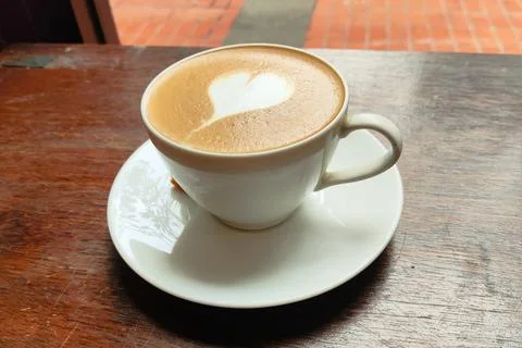 A white coffee cup with a heart drawn on it sits on a wooden table Stock Photos