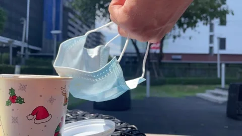 White coffee cup on interlace weave table sunny windy,hand holding surgical mask Stock Footage 251845450