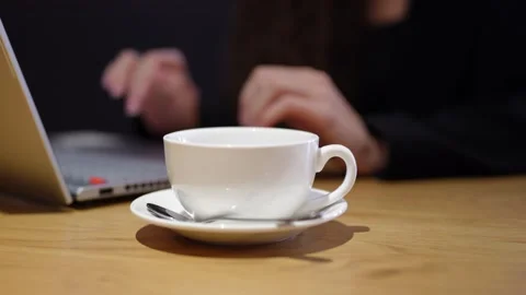 A white coffee cup sits on a table, while a person types on a laptop Stock Footage 292906888