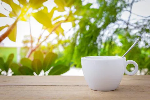 A white coffee cup with spoon is placed on a wooden plate and on the landscap Stock Photos