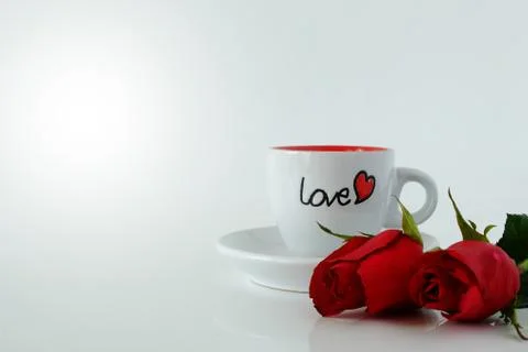 White coffee cup with word LOVE and couple of roses on white background. Stock Photos
