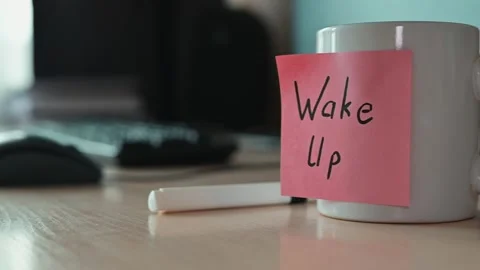 A white coffee mug sits on a desk with a pink sticky note that says Wake Up. A Video stock 339094020