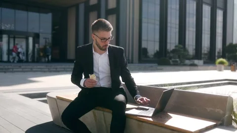 White Collar Worker Typing on Laptop While Eating Lunch on a City Bench Vídeo Stock 330795311