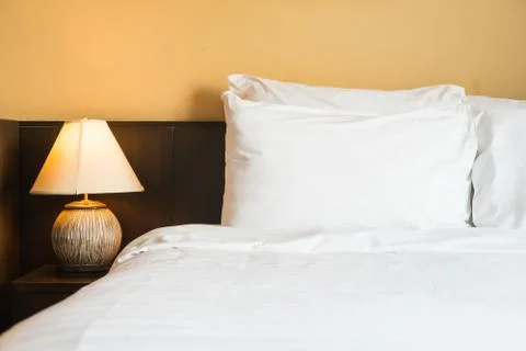White comfortable pillow on bed with light lamp Stock Photos