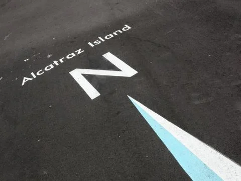 White compass arrow on asphalt pointing north towards Alcatraz. Stock Photos
