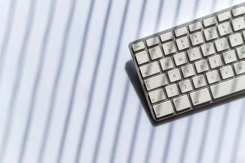 White computer keyboard on desk with dramatic shadow stripes, minimal desig.. 写真素材