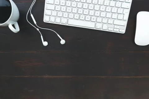 White computer keyboard mouse earphones and coffee cup on dark brown table ba Stock Photos