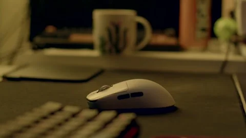White computer mouse on dark deskpad as hand reaches in evening glow Stockbeeldmateriaal 347204311