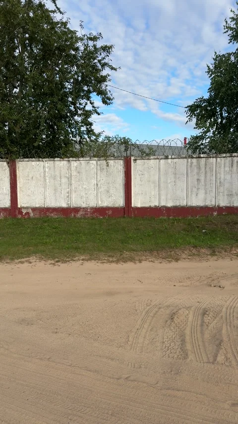 White concrete fence with red posts and barbed wire near a sandy road Видео 341702575