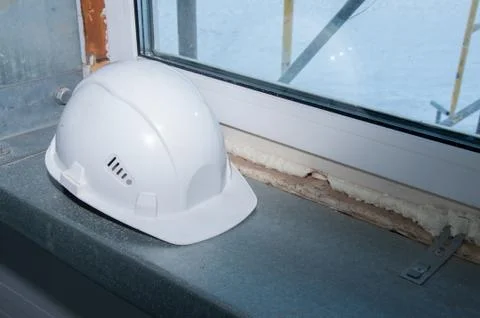 White construction helmet of a construction worker on a window background Stock Photos