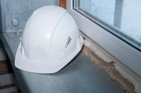 White construction helmet of a construction worker on a window background Stock Photos