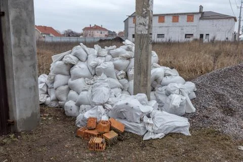 White construction sacks of construction waste are dumped in heap near fence  Stock Photos