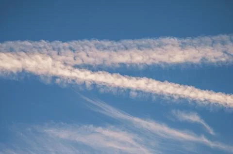 White contrails and wispy clouds forming parallel lines across a clear blue s 스톡 사진