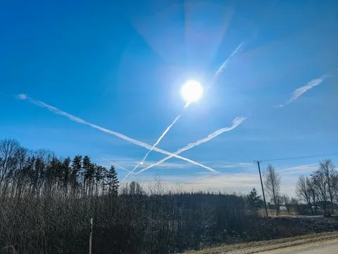White contrails form an X pattern in the clear blue sky as the sun. Foto stock