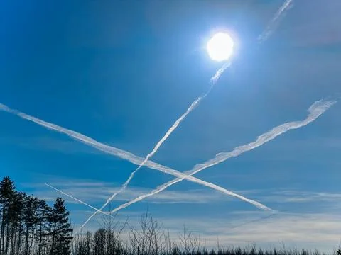 White contrails form an X pattern in the clear blue sky as the sun. Foto stock