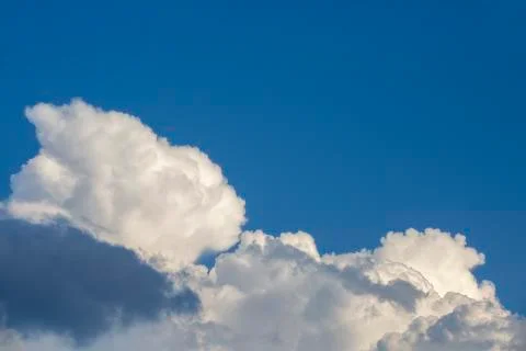 White contrasting clouds backlit by the sun on a blue summer sky. Background. Stock Photos