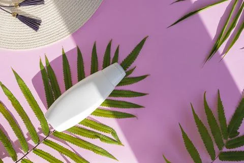 White cosmetic bottle container with palm leaf and white cap on pink paper ba Stock Photos