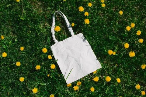 White cotton or mesh bag on dandelion green grass background. Zero waste, no Photos