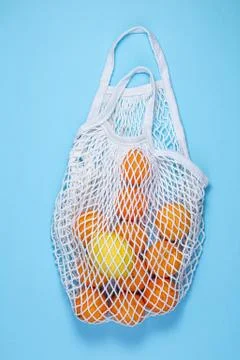 A white cotton string bag with tangerines and lemon lies on a blue background Stock Photos