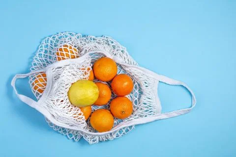 A white cotton string bag with tangerines and lemon lies on a blue background Foto stock
