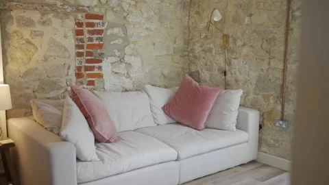 A white couch with pink pillows sits in front of a brick wall Stock Footage 302442189