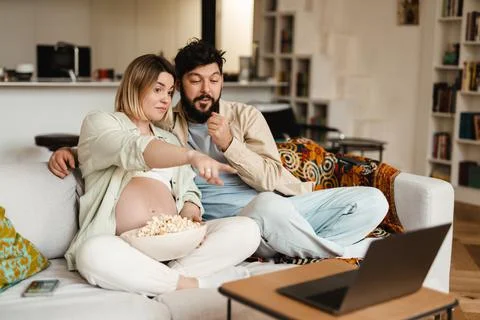 White couple eating popcorn while watching movie on laptop at home Foto stock