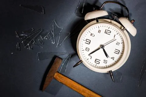White crashed alarm clock, shards of glass and hammer on grey background. Stock Photos