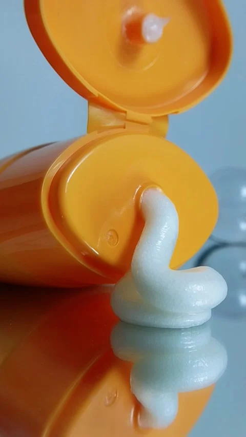 White cream coming out of orange packaging product on glass reflection. Stock Footage 335388341