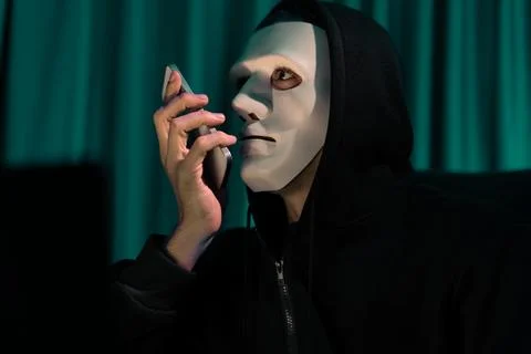 White criminal anonymous mask calling to IT owner to threaten ransom. Pecuniary. Foto stock