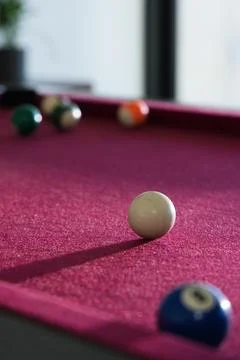 White cue ball sitting sharp on burgundy felt pool table near vertical window, 库存照片