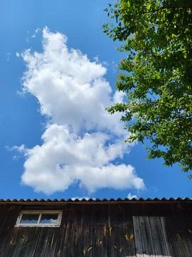 White cumulus clouds over the edge of a house roof Stock Photos