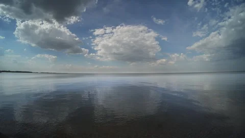 White cumulus clouds reflecting in a large calm lake with small wave distorting Stock Footage 335898188