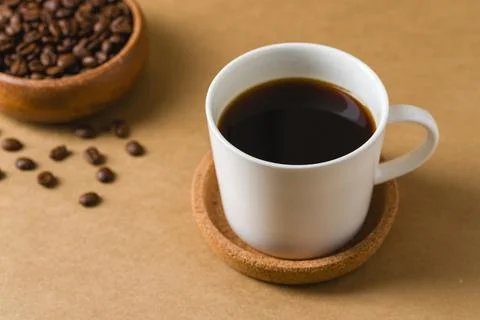 White cup of black coffee with roasted beans and bowl on warm background Stock Photos