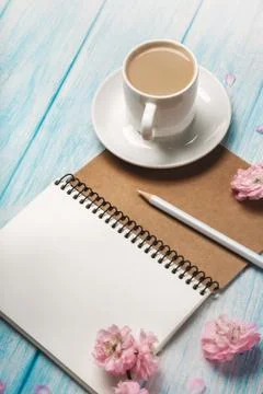 White cup cappuccino with sakura flowers, notebook on a blue wooden table Stock Photos