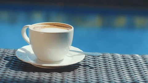 White cup of cappuccino on wicker table with blue water background Stock Footage 81606096