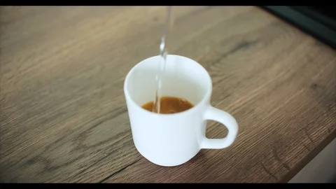 White cup of coffee and kitchen with wooden top. Pouring  from kettle Video stock 93984798