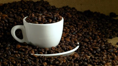 White cup with coffee beans, fried coffee beans on burlap Stock Footage 85594875