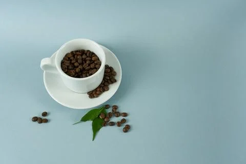 White cup with coffee beans on gray background with space for text. Stock Photos