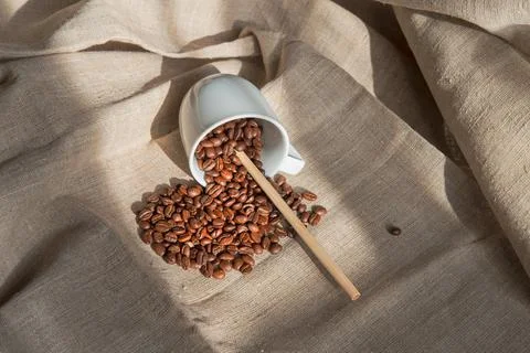 A white cup with coffee beans in it and a bamboo tube lies on a light canvas Stock Photos