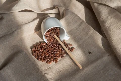 A white cup with coffee beans in it and a bamboo tube lies on a light canvas Stock Photos