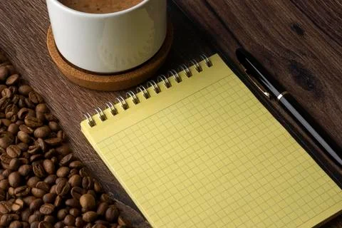 White cup of coffee, a blank notebook, a pen and roasted coffee beans Stock-Fotos