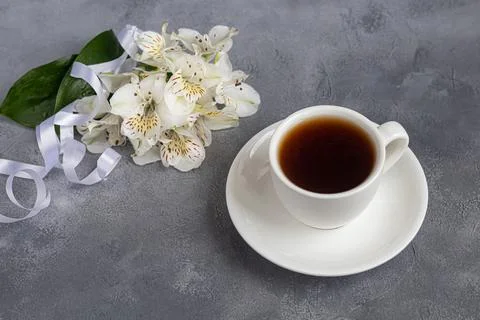 White cup with coffee on a gray background. A bouquet of orchids entwined wit Stock Photos