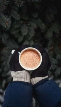 White cup of coffee in the hands dressed in gloves on the background of the C Stock Photos
