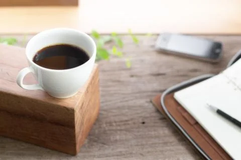 White cup coffee with note book smart phone on wooden top table Stock Photos