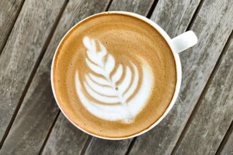 White cup of coffee with pattern on top of foam, against background of wooden Stock Photos