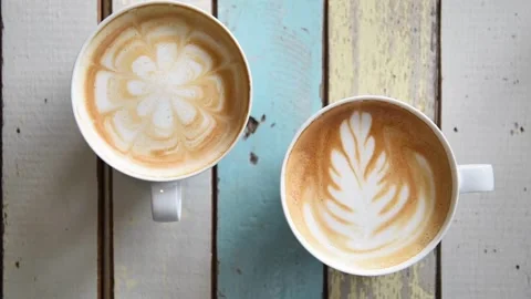 White cup of coffee served with latte art on the table at coffee shop, top shot. 動画素材 334650859