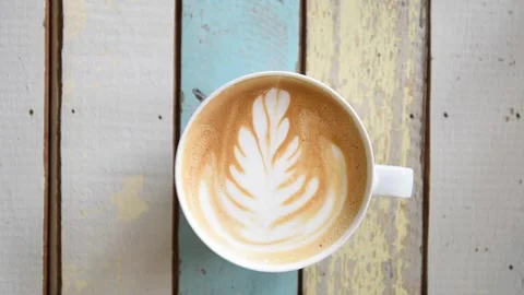 White cup of coffee served with latte art on the table at coffee shop, top shot. 動画素材 334650880